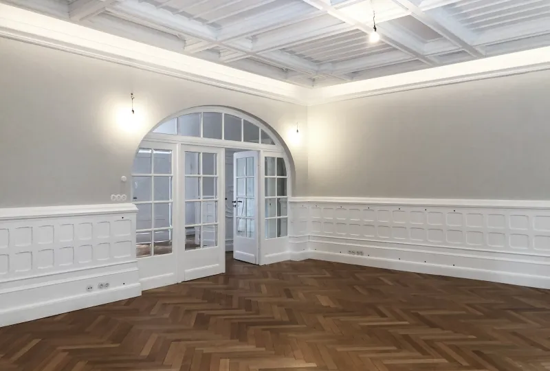 Sanierter Wohnraum der Stadtvilla R mit weißer Kassettendecke, Wandvertäfelung, Fischgrätparkett und Rundbogentür