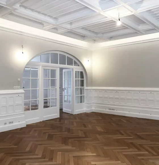 Sanierter Wohnraum der Stadtvilla R mit weißer Kassettendecke, Wandvertäfelung, Fischgrätparkett und Rundbogentür